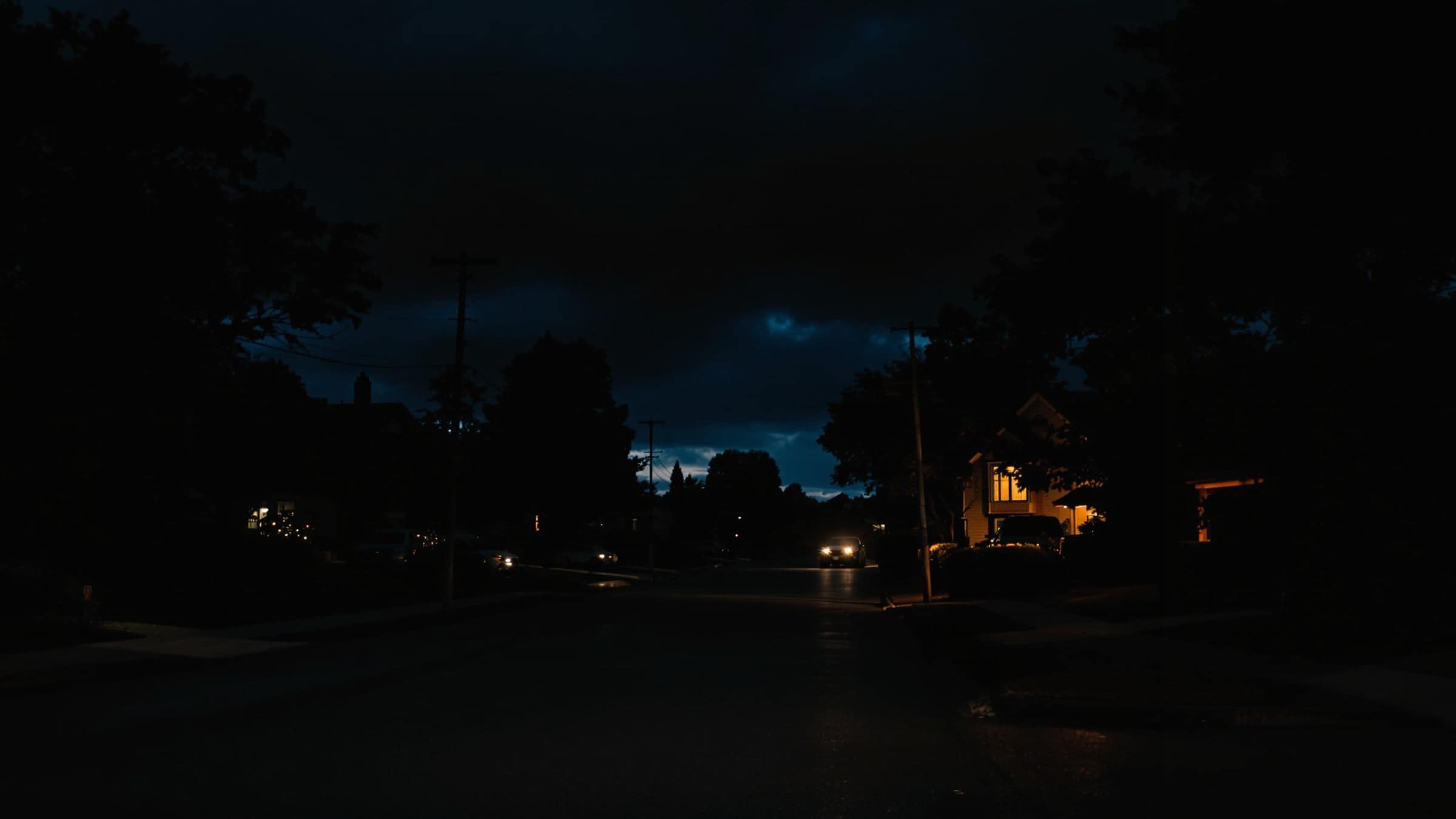A dark street during a power outage with one window lit.